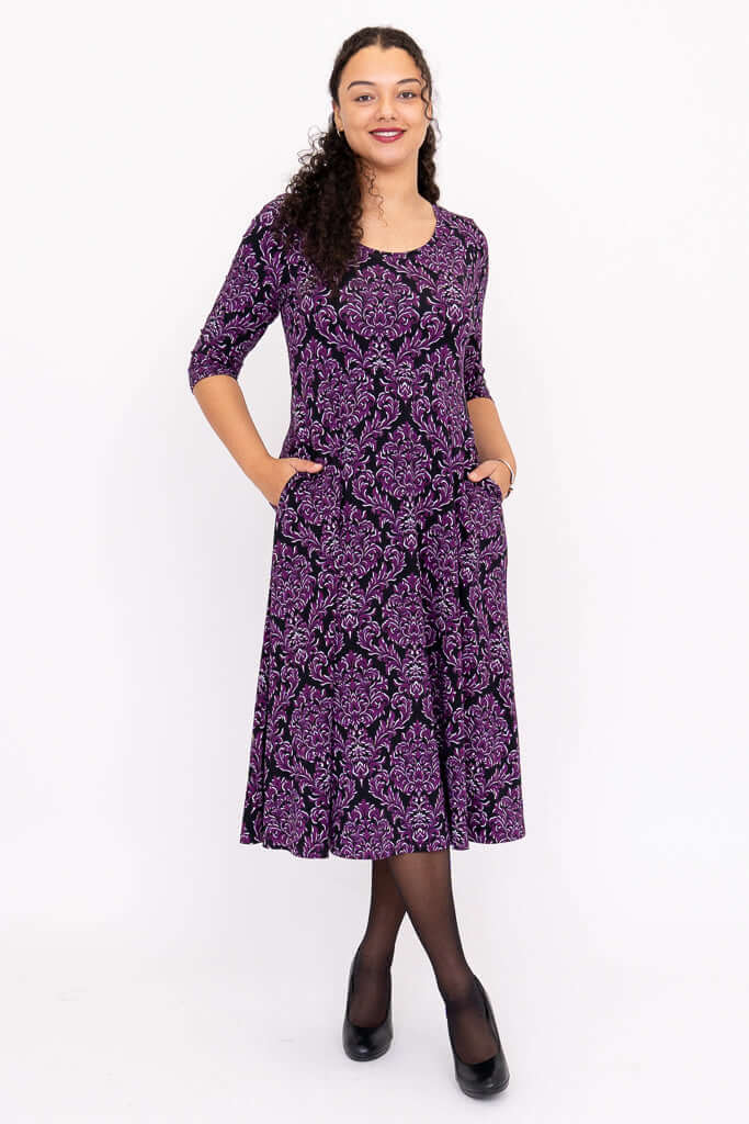 Model showing pockets of purple damask midi dress with three-quarter sleeves