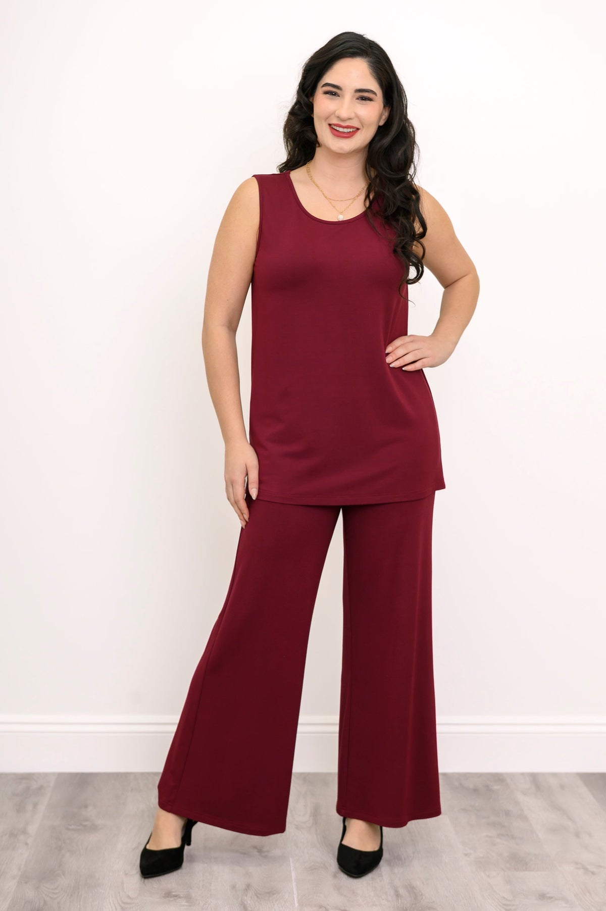 Full-length view of a woman walking in a burgundy sleeveless tank top and matching knit pants.