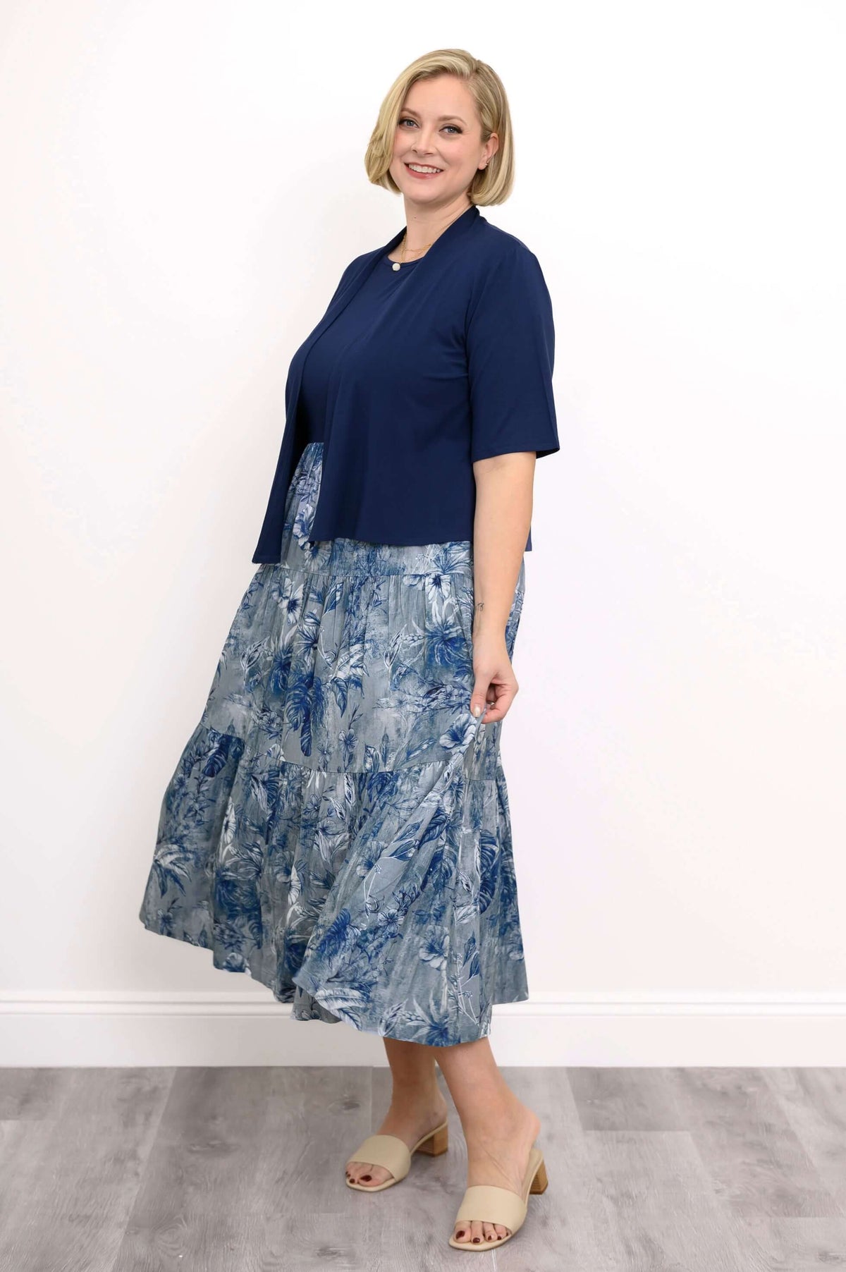 Woman in a navy floral midi dress shown with a navy short-sleeve cardigan, side profile