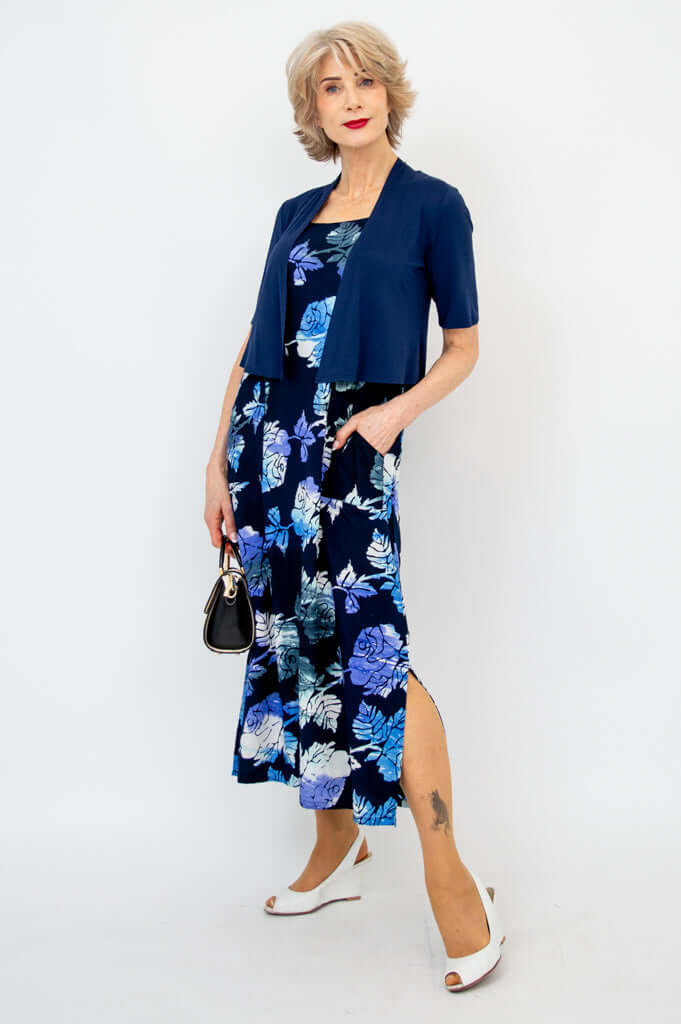 Woman in a navy blue floral dress styled with a short sleeve navy shrug and black handbag