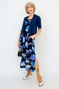Woman in a navy blue floral dress styled with a short sleeve navy shrug and black handbag