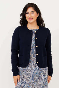 Angled front view of woman in navy cardigan with gold buttons over a paisley dress