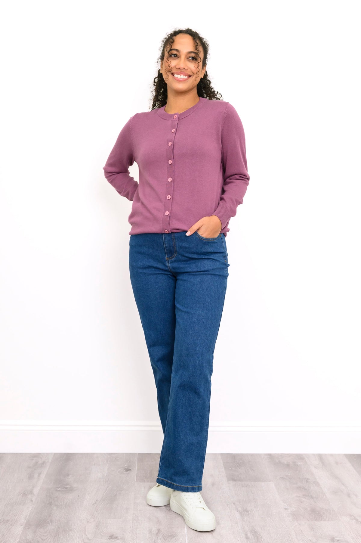 Front view of a woman wearing a pink crewneck button up cardigan styled with dark wash denim pants.