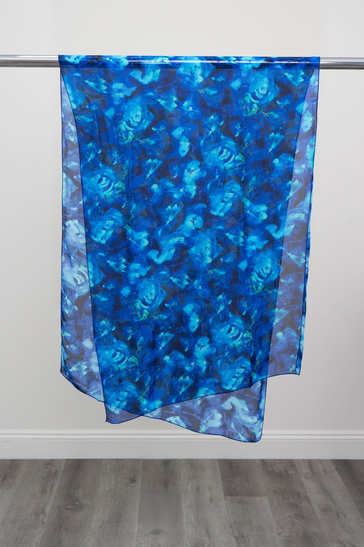A large silk scarf with a watercolour blue print displayed on a metal rod against a white background, front view