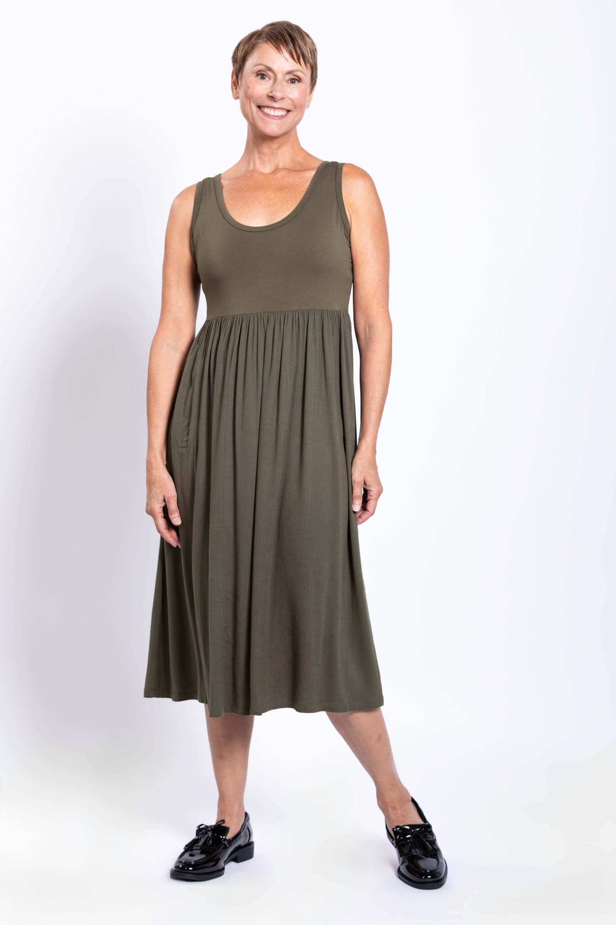 Woman wearing an olive empire waist midi dress and black shoes, smiling