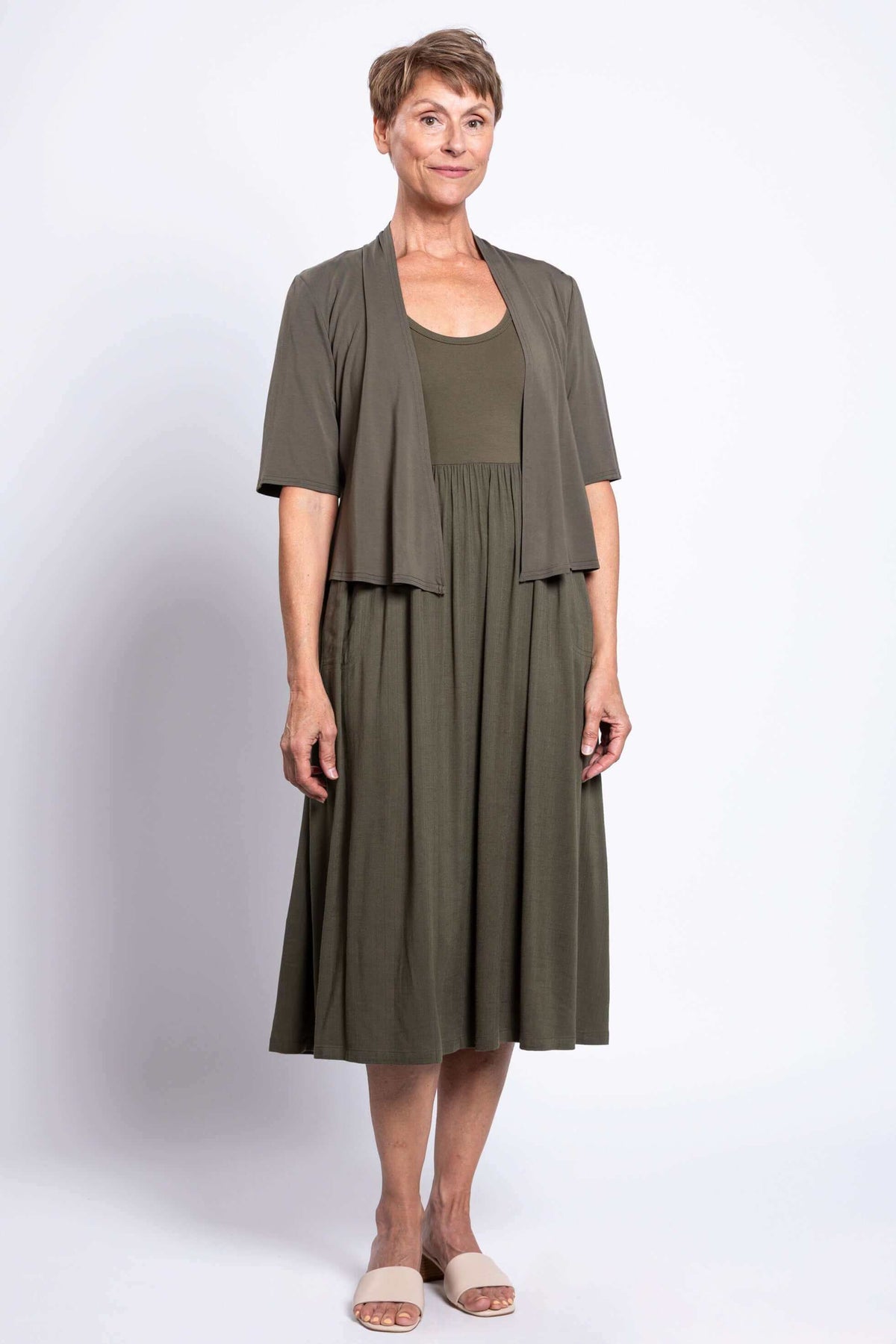 Woman layering olive open cardigan over empire waist midi dress