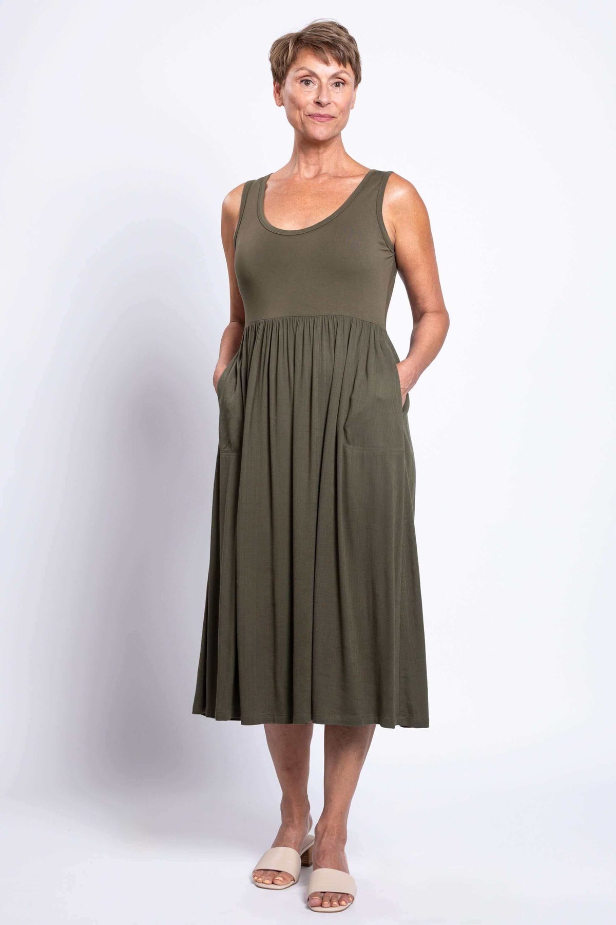 Woman showing pockets of olive empire waist midi dress with light sandals