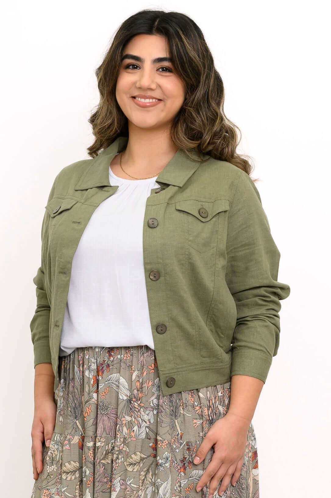 Woman wearing an olive green linen blend jacket over a white top and floral skirt