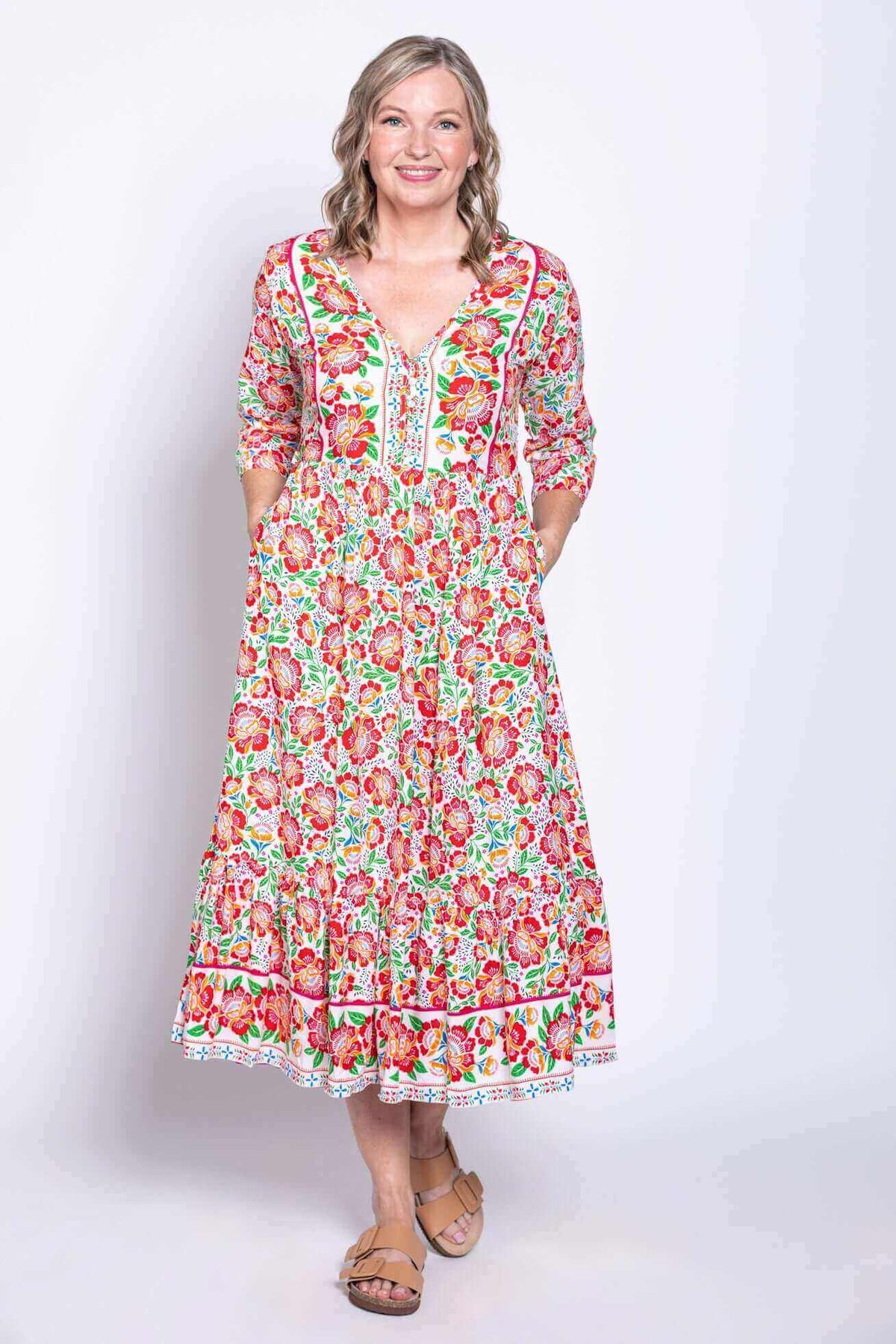 Woman in vibrant floral midi dress with hands in pockets, facing forward