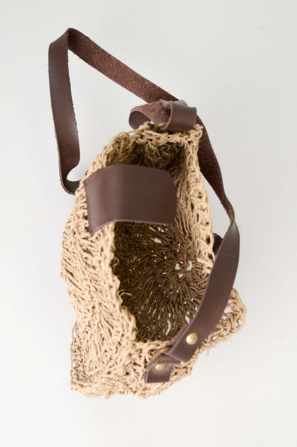 Top view of open round rattan bag, showing spacious interior and brown leather strap