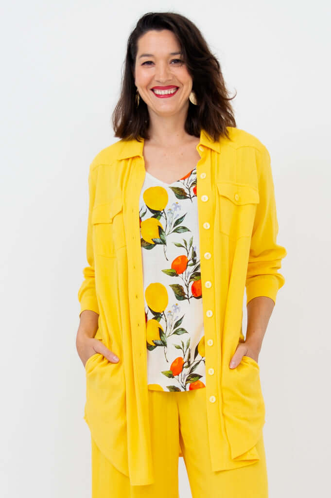 Woman wearing yellow button-up tunic open over a citrus print top and matching yellow pants