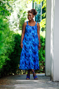 Woman in blue floral jumpsuit standing outdoors with greenery