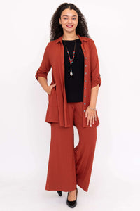 Woman in rust wide leg pants and matching shirt, black top, and black pumps