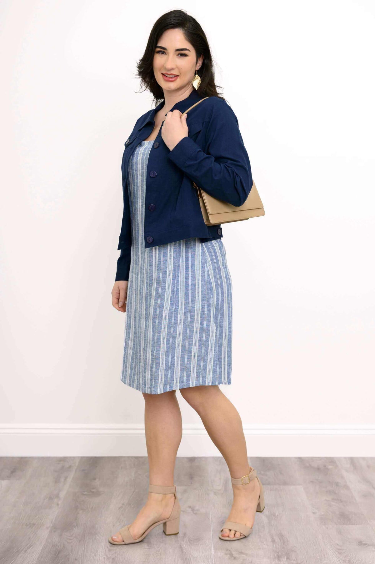 Woman holding a tan purse, blue striped shift dress and navy jacket