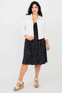 Front view of woman in black polka dot dress paired with a white jacket