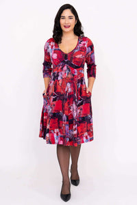 Woman smiling with hands in pockets, modeling a red and purple floral fit and flare dress