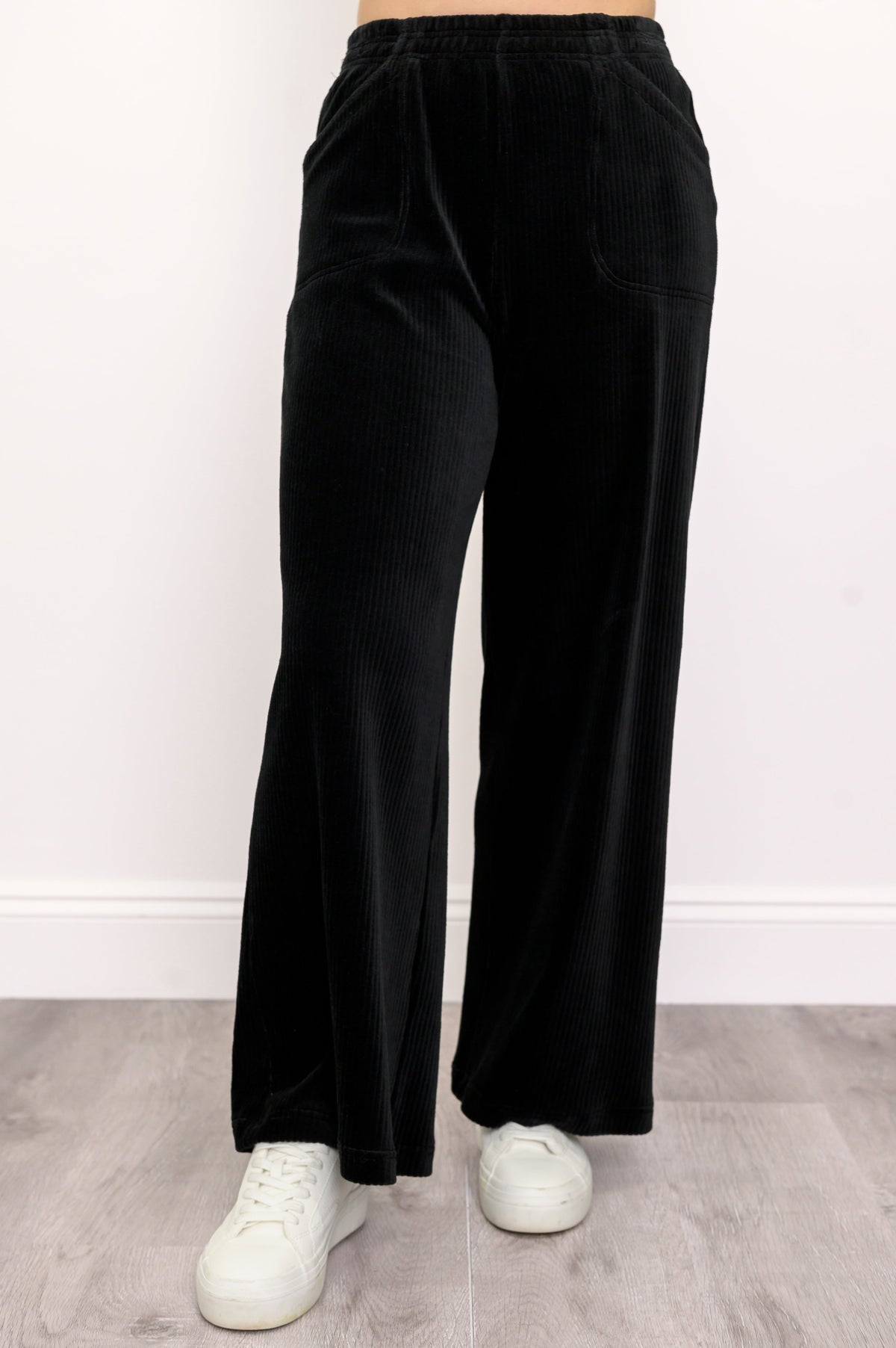 Woman wearing black wide-leg corduroy pants and white shoes on a white background, front view