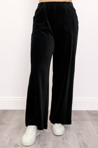 Woman wearing black wide-leg corduroy pants and white shoes on a white background, front view
