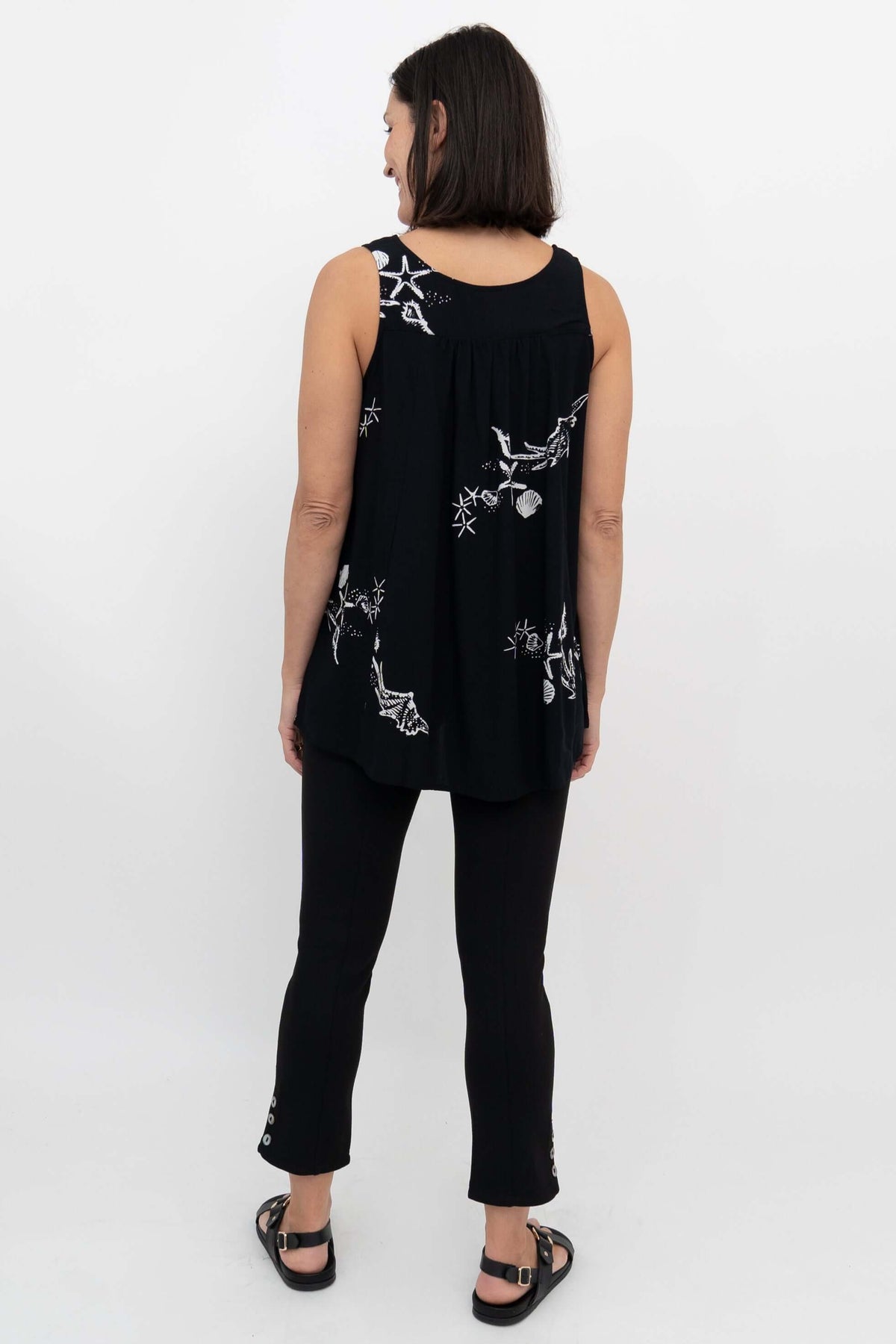 Back view of woman in a black flowy tank top with white shell and starfish pattern