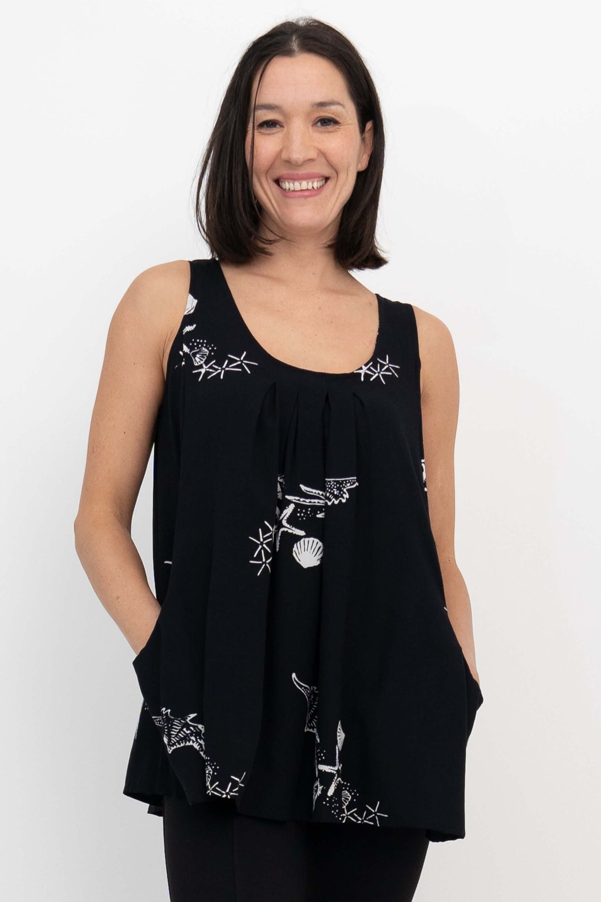 Woman wearing a black tank top with white shell and starfish print, front view
