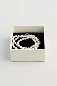 Pearl necklace neatly arranged in a cream gift box with black interior