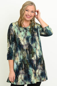 Smiling woman wearing a blue-green watercolor forest print A-line tunic with 3/4 sleeves, front view.