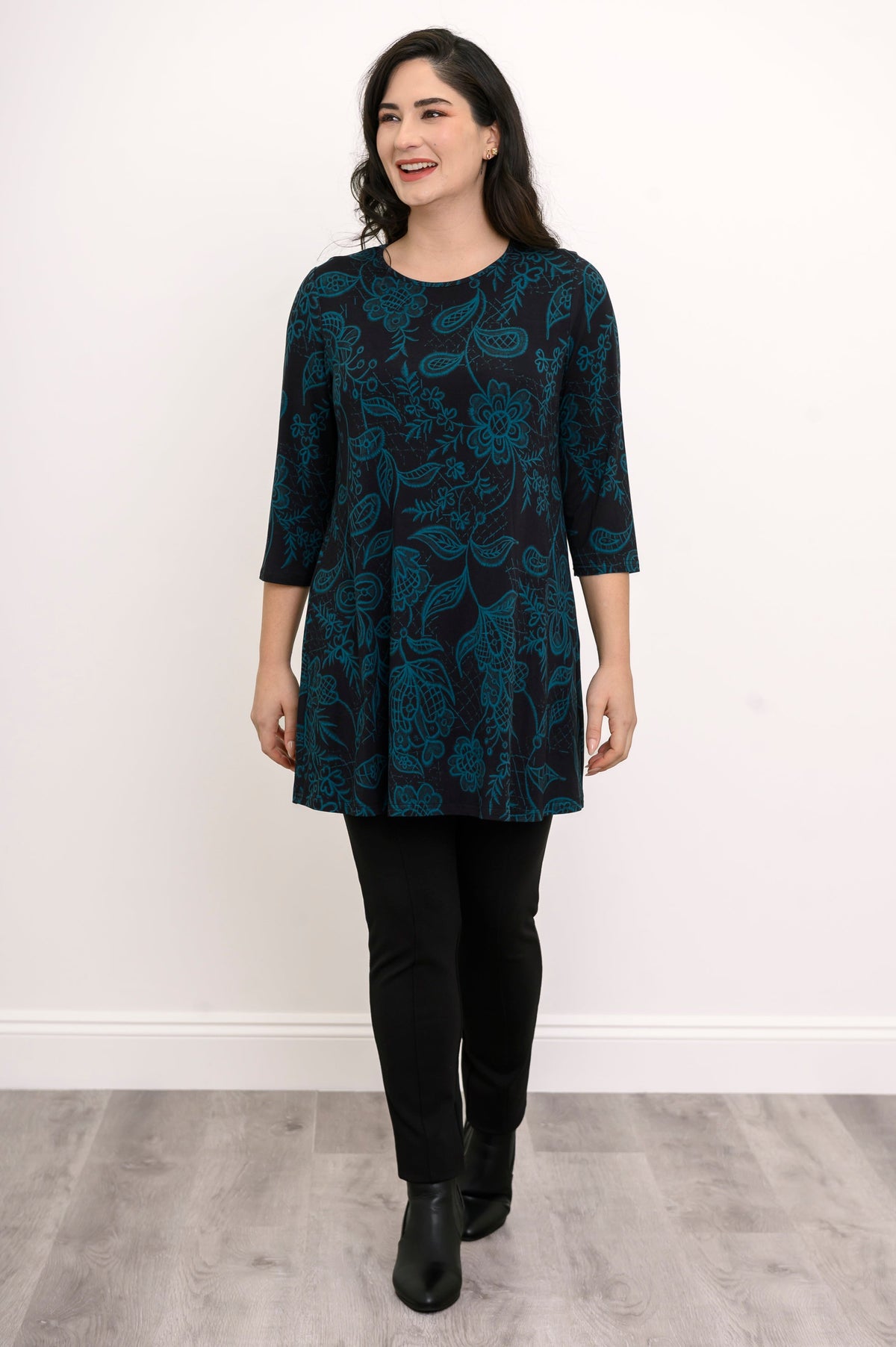 Women's three-quarter sleeve knit tunic in a dark floral print, paired with black trousers in a casual pose.