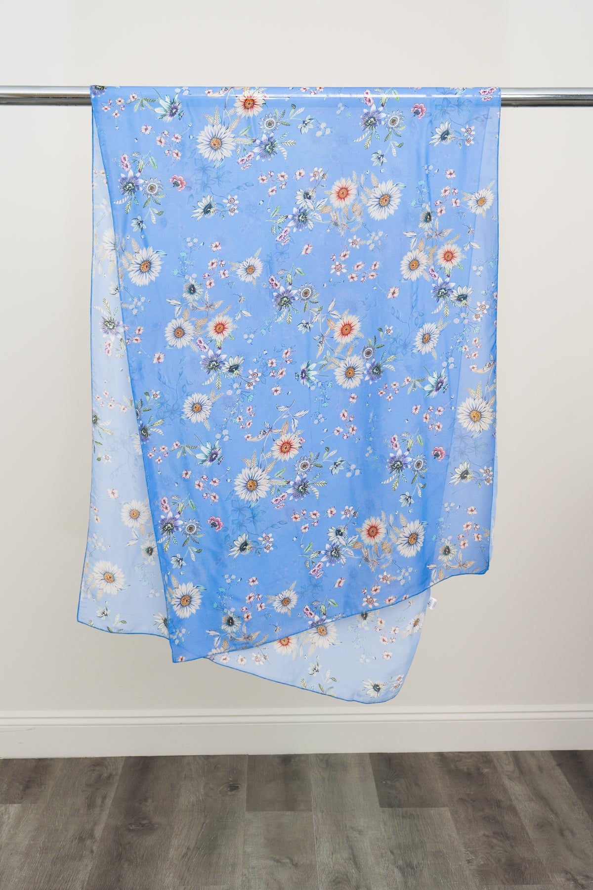 A large blue silk scarf with a daisy pattern displayed on a metal rod against a white background, front view