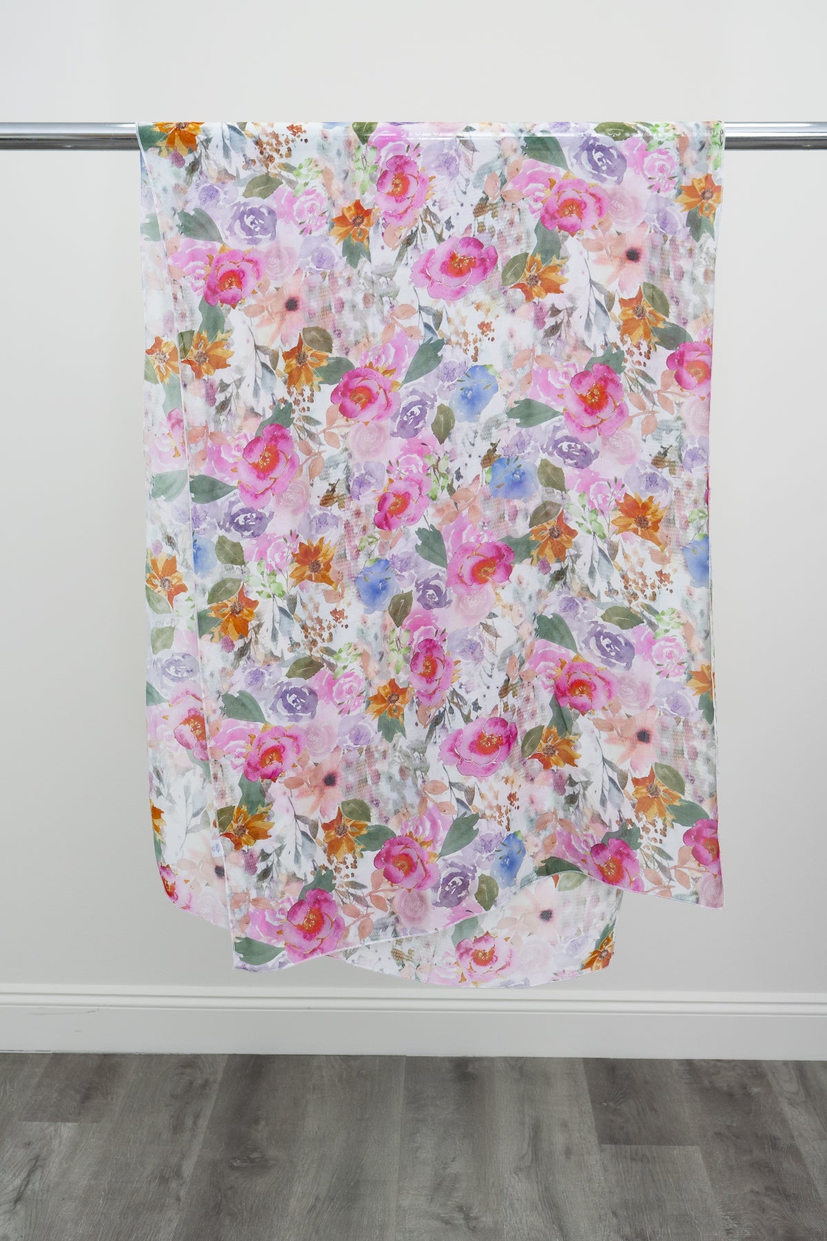 A large silk scarf with a pink and multicolour floral pattern displayed on a metal rod against a white background, front view