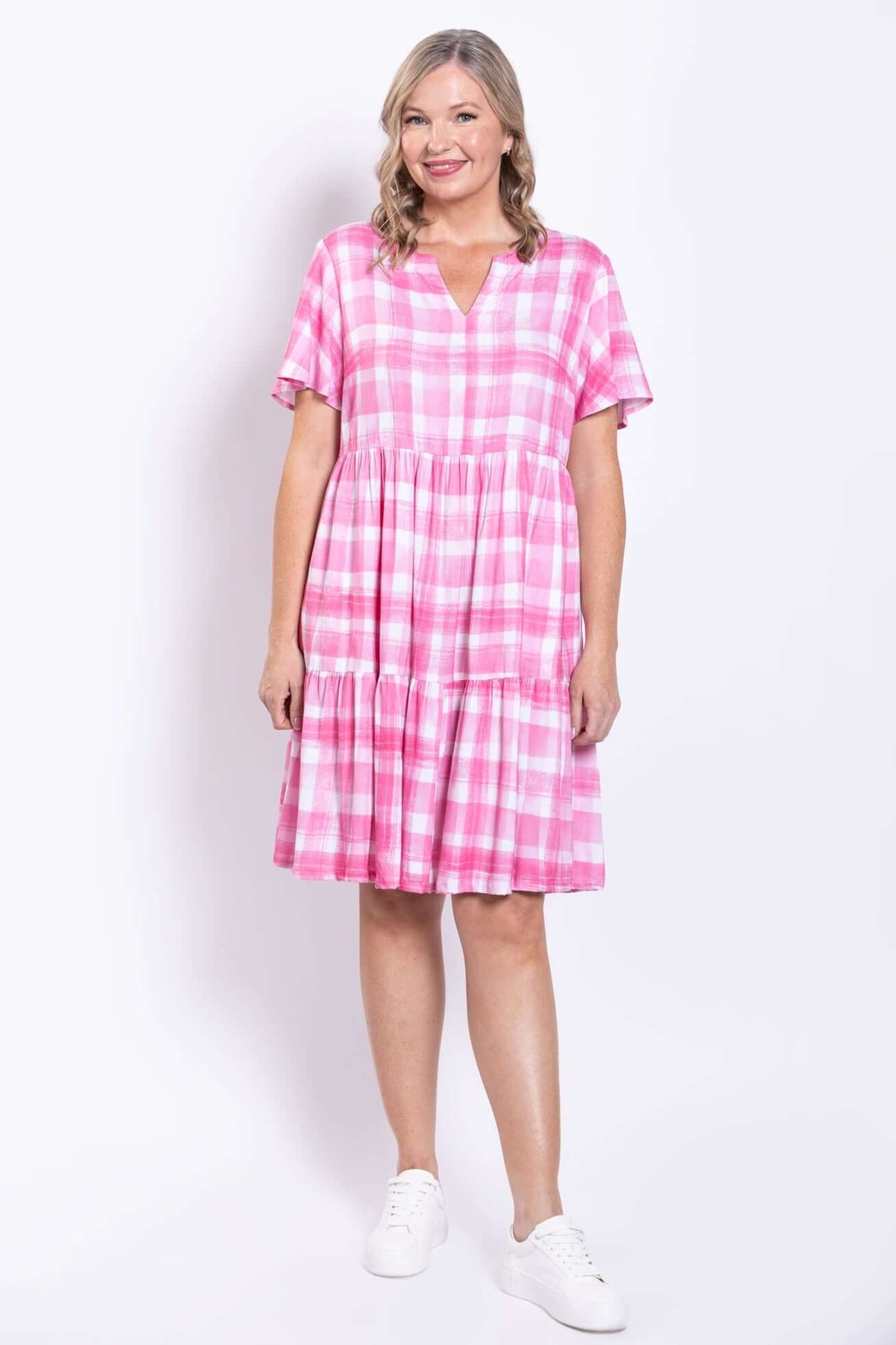 Front view of woman smiling in pink checkered dress with white sneakers