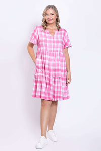 Woman with hand in pocket wearing above-knee pink gingham dress, front angle