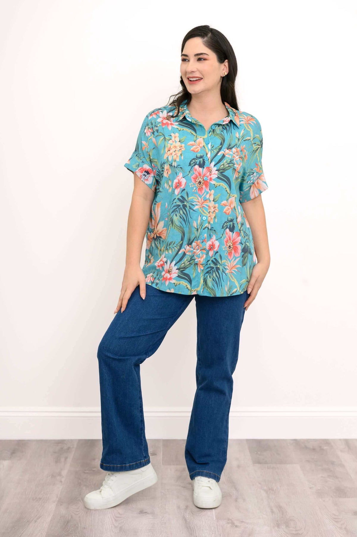 Woman smiling in a turquoise floral blouse with jeans in a playful pose