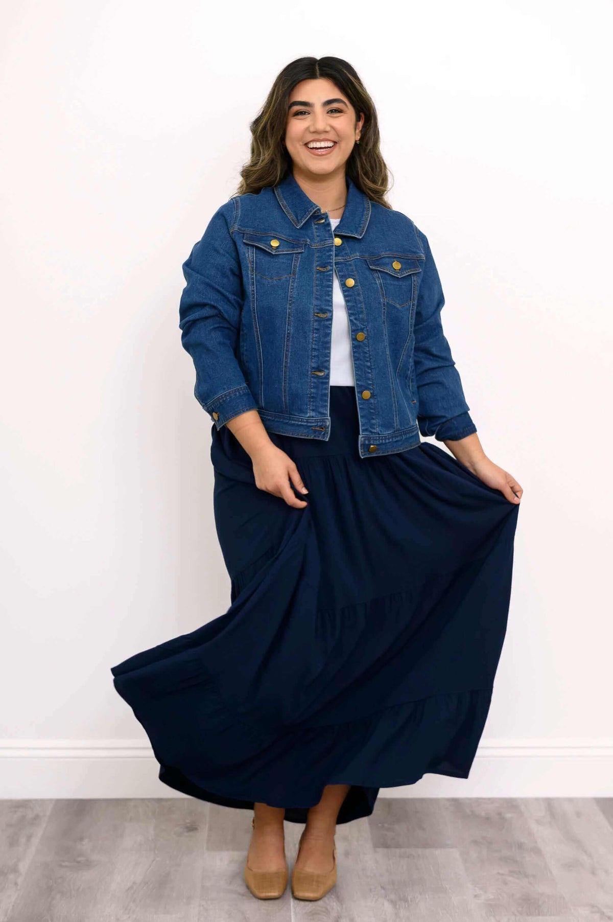 Model holding navy tiered maxi skirt playfully, wearing denim jacket and white top