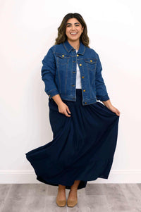 Model holding navy tiered maxi skirt playfully, wearing denim jacket and white top