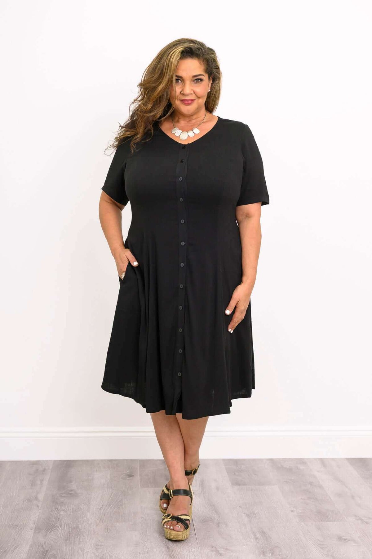 Plus-size woman in a black button-up dress with pockets and statement necklace, front view