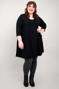Plus size model posing with hand on hip in black A-line tunic dress