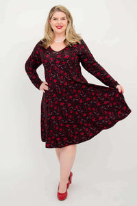 Plus size woman holding out skirt of black and red floral fit and flare dress