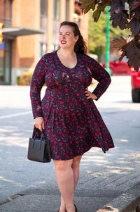 Plus size woman outdoors in black and red floral fit and flare dress, holding a handbag
