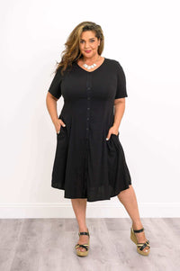 Plus size woman posing in black dress with pockets and platform sandals