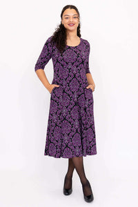 Model with hands in pockets wearing a purple damask midi dress