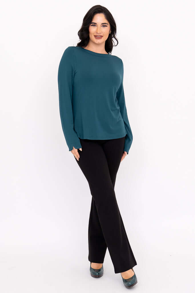 Woman modeling teal boat neck top with hands in front and black pants