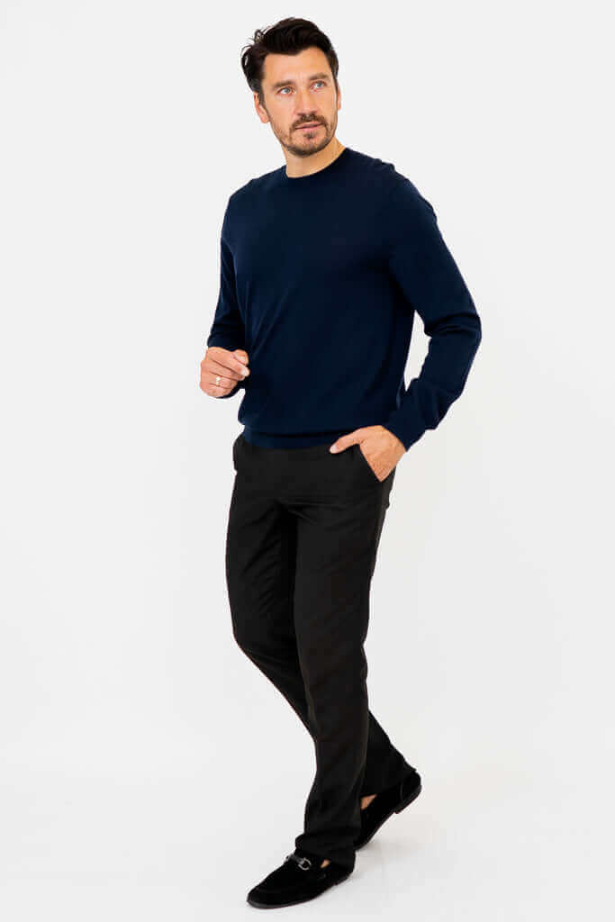 Man in navy sweater and black pants, posing with one hand in pocket