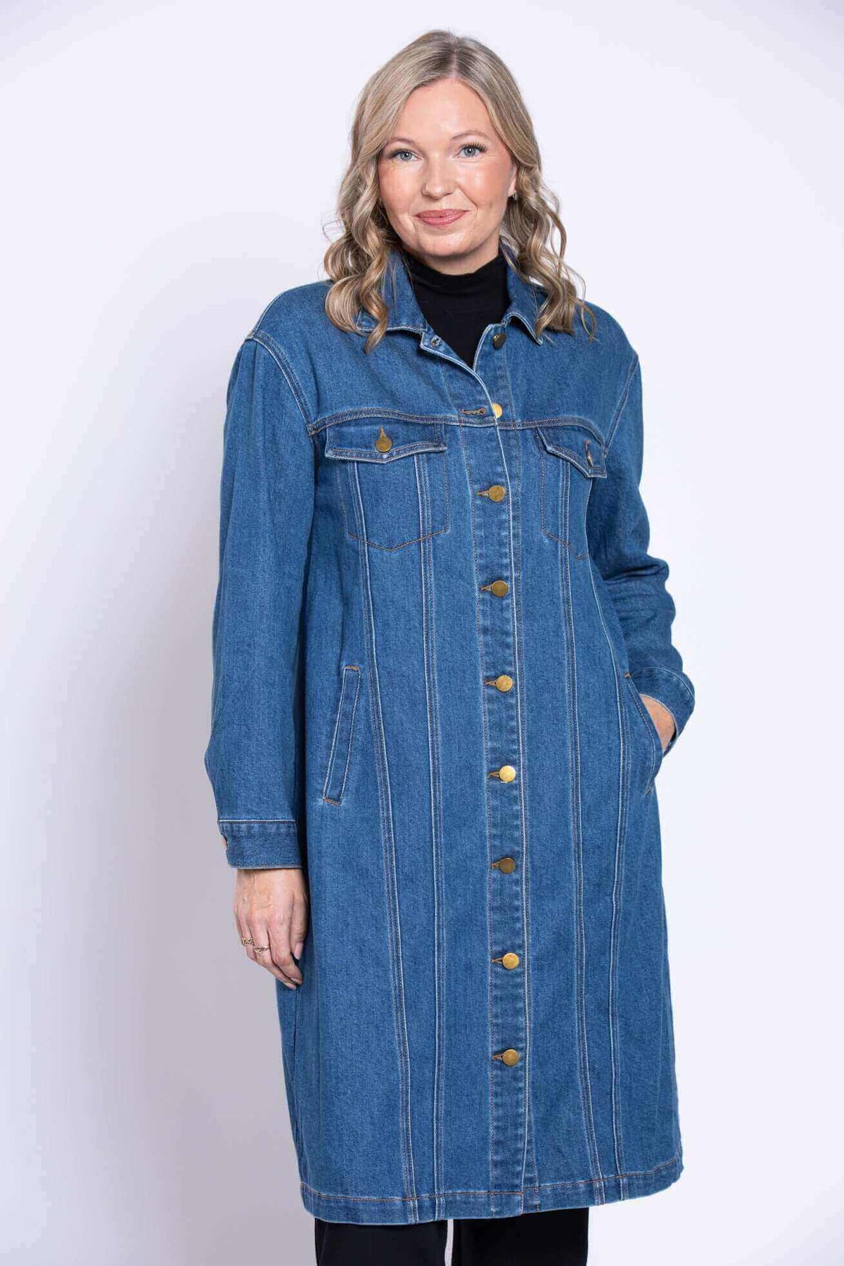 Woman posing hands in pockets wearing a long blue denim jacket
