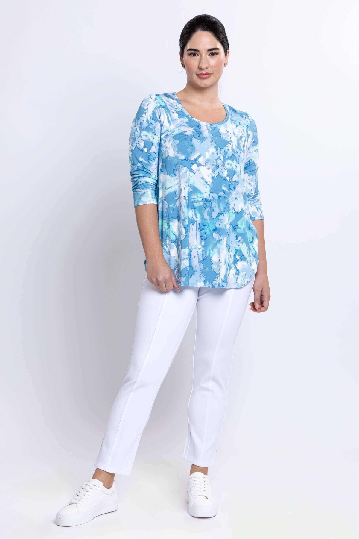 Model posing in blue watercolor Jazz Top with white pants and sneakers