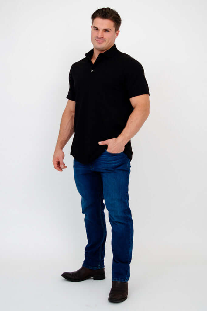 Man posing with hand in pocket in black bamboo polo shirt and blue jeans