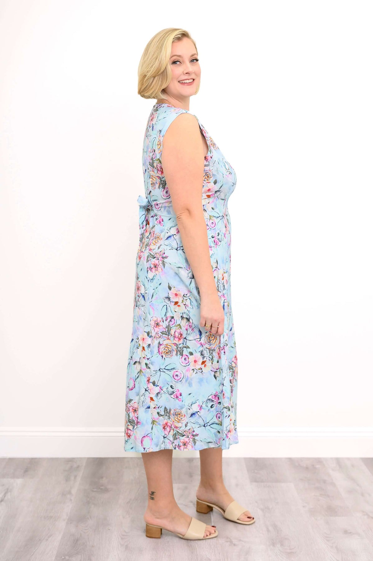 Profile view of a woman in a sleeveless blue floral midi dress with tie-back detail