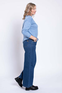 Side view of woman in blue wide leg jeans and light blue sweater with hands in pockets