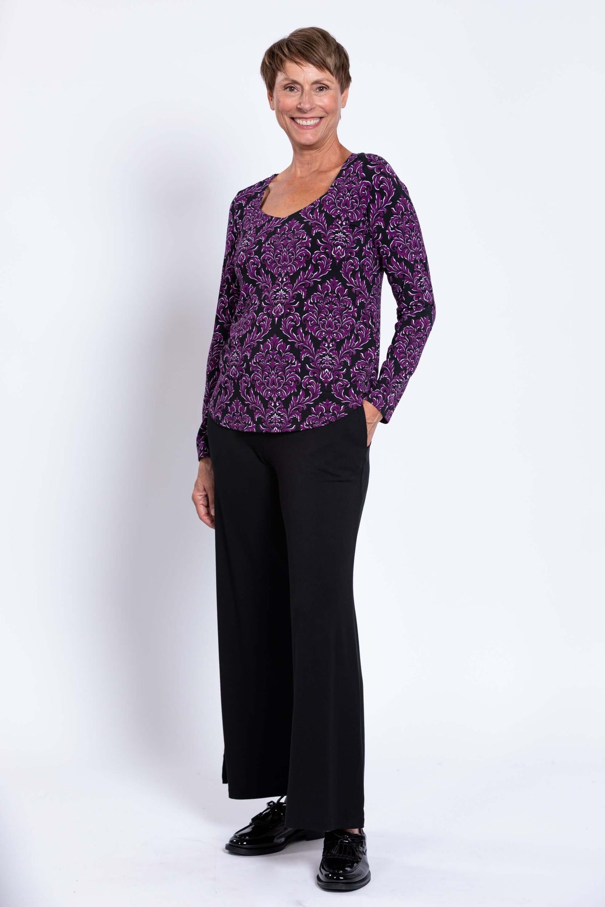 Full body front view of model in purple patterned top and black wide-leg pants