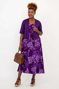 Model in purple floral dress with jacket, holding a brown handbag
