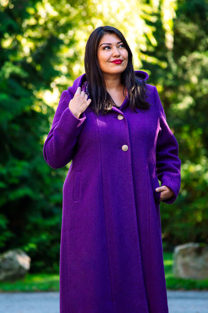 Woman outdoors in a purple hooded coat with buttons, hands by collar and pocket